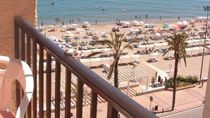 Een strand met parasols, mensen, een heldere lucht en boten in het water.
