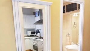 Een kamer met een witte console tafel, een spiegel erboven en uitzicht op een keuken met witte kastjes en een magnetron.