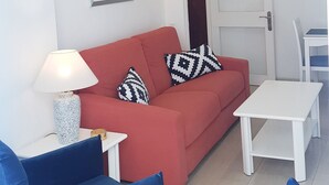 Een woonkamer met een rode bank, blauwe stoelen, een witte tafel en een plafondventilator.