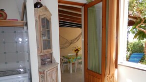A kitchen with a stove, a cabinet with a glass door, and a dining area with a table and chairs. - Casa Catalogna A, Historic Center of Lipari (Lipari)