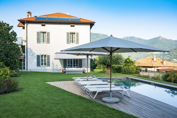 Ein modernes Haus mit Swimmingpool, einer Sonnenterrasse und großen Sonnenschirm.