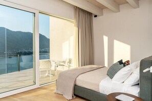 Ein Schlafzimmer mit einer großen Schiebeglastür, die auf einen Balkon mit Blick auf Berge und einen See führt.