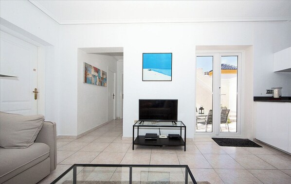 A modern living room with a sofa, a glass coffee table, a flat-screen TV, and a painting on the wall.