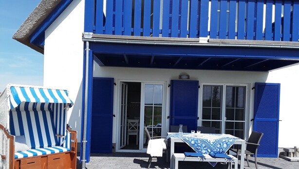 Un edificio blu e bianco con un balcone, un tavolo con sedie e una sedia da spiaggia a righe.