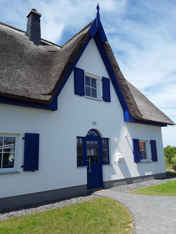 A white building with blue shutters and a thatched roof. - Cozy, modern, child-friendly vacation home with large garden (Vaschwitz)
