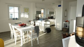 Una cucina moderna con mobili bianchi, un'area pranzo con sedie bianche e un'ampia finestra che offre luce naturale.