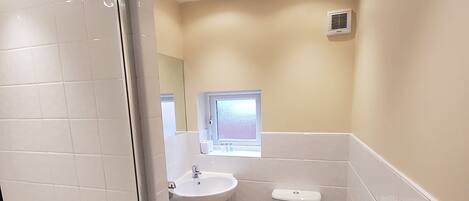 Un bagno con piastrelle bianche, un lavandino, un water e una zona doccia.