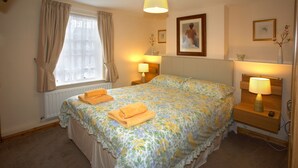 A bedroom with a bed, two bedside lamps, a window with curtains, and a radiator. - Saltburn Holidays Primrose Cottage (Guisborough)