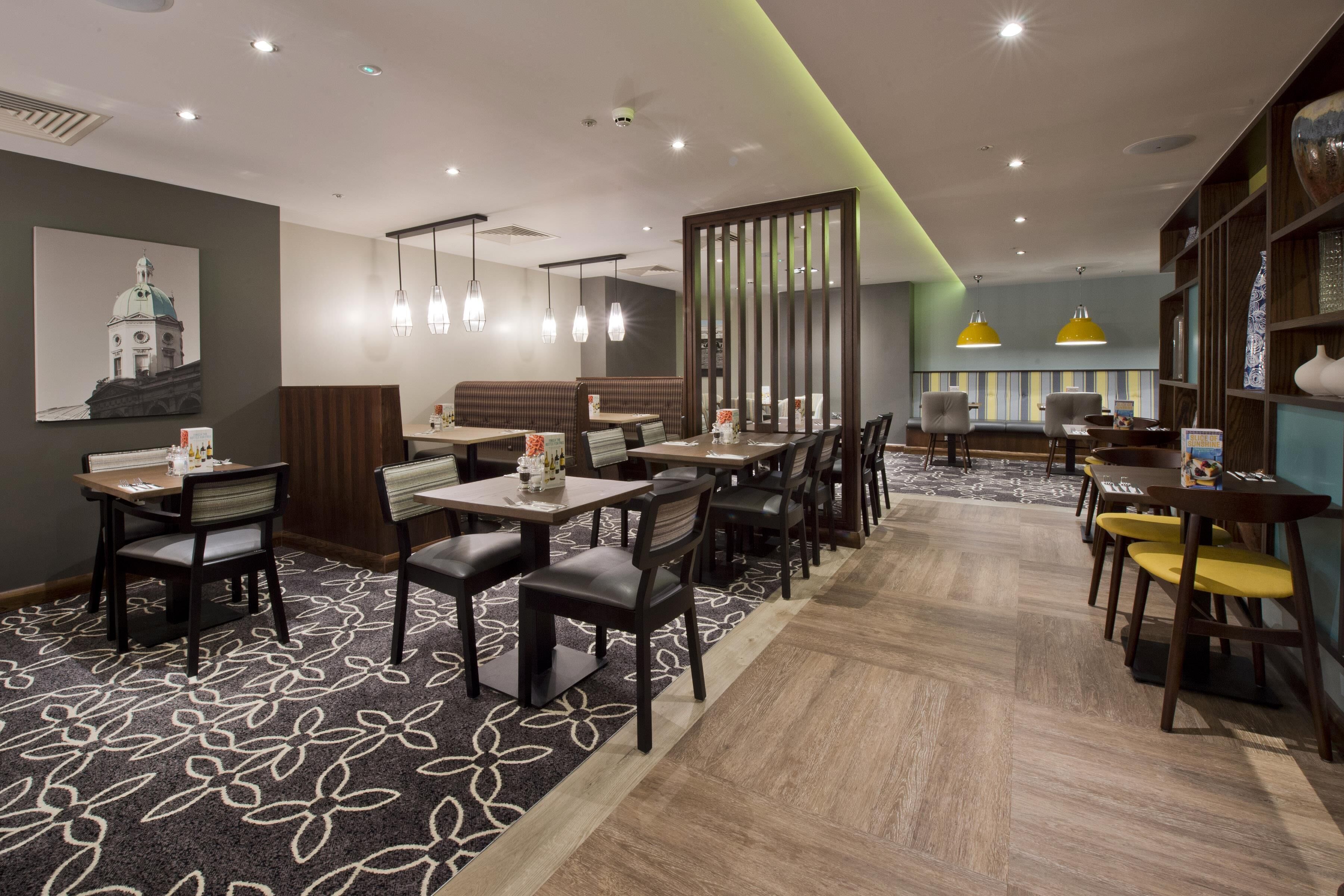 A restaurant with booths, tables, and chairs, featuring a patterned carpet and pendant lighting.