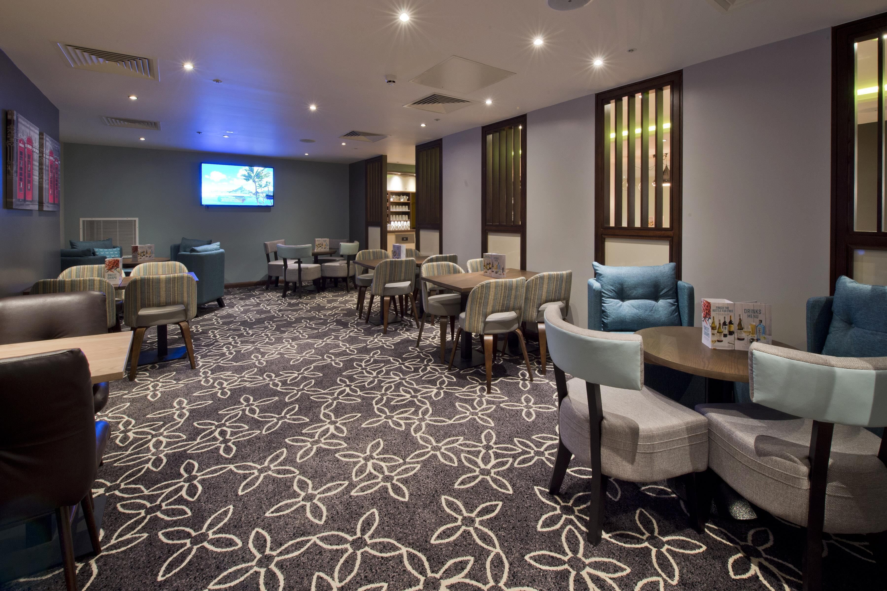 A hotel room with a carpeted floor, a flat-screen TV, multiple seating areas, and a bar area.