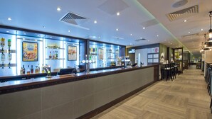 A bar area with a long counter, shelves with bottles, and a tiled floor. - Premier Inn London Farringdon - Smithfield (London)