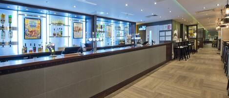A bar area with a long counter, shelves with bottles, and a tiled floor.