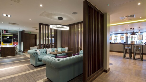 A modern lobby with a sectional sofa, a round table, and a bar area. - Premier Inn London Farringdon - Smithfield (London)