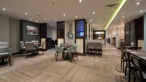 A hotel lobby with a modern design, featuring a central seating area with tables and chairs, a reception desk, and a visible staircase leading to other floors. - Premier Inn London Farringdon - Smithfield (London)