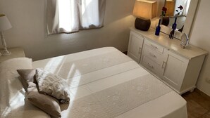 Un lit bien fait, avec des oreillers, une lampe de chevet, une commode avec un miroir et une fenêtre avec des rideaux.