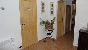 A hallway with a wooden door, a small table with a basket of flowers, and a tiled floor.