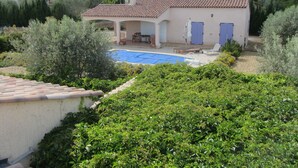 A house with a swimming pool, surrounded by greenery and other houses in the background.