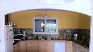 A compact kitchen with wooden cabinets, a built-in oven, microwave, and dishwasher. A window above the sink provides natural light.