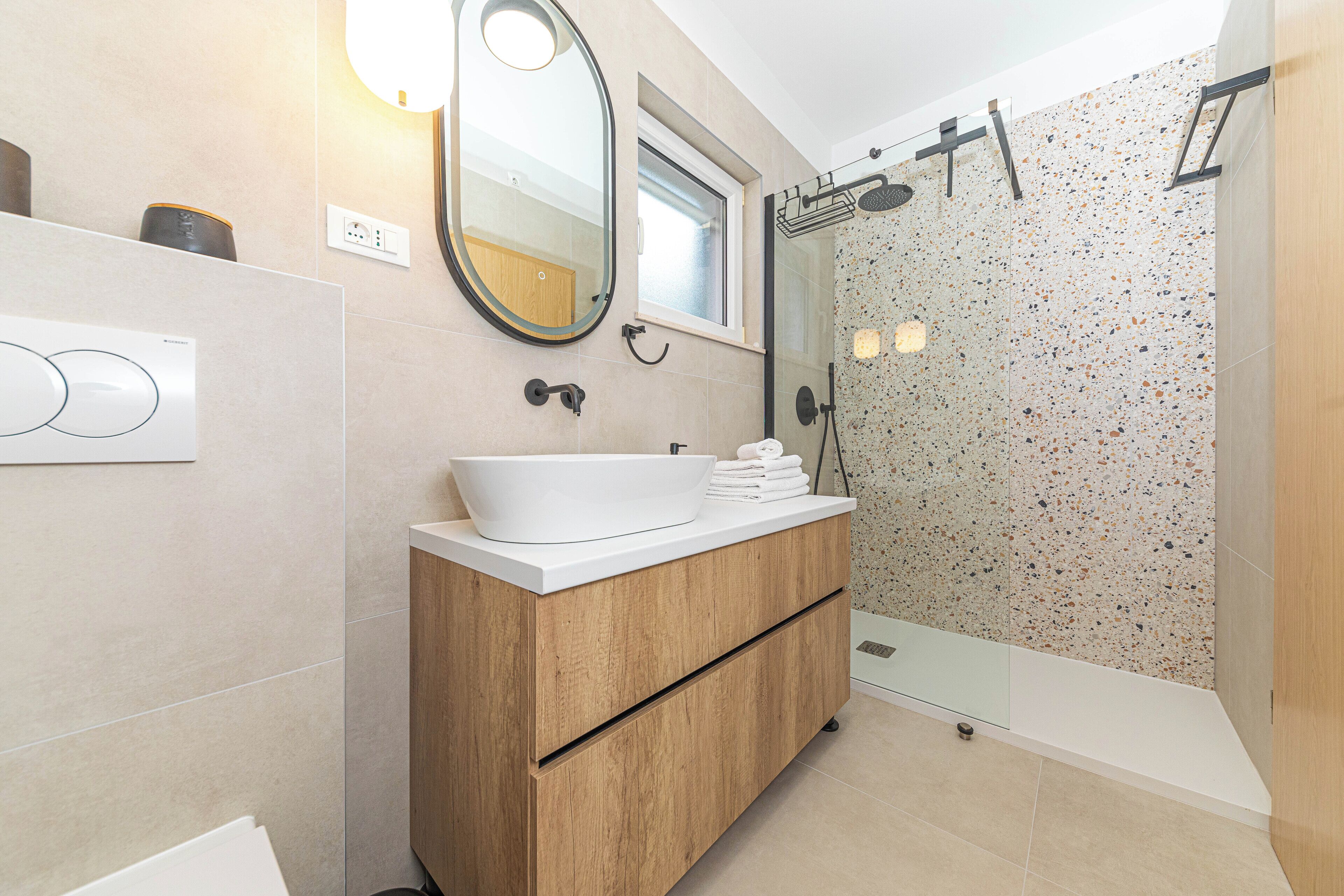 A modern bathroom with a wooden vanity, a white sink, and a glass shower enclosure.