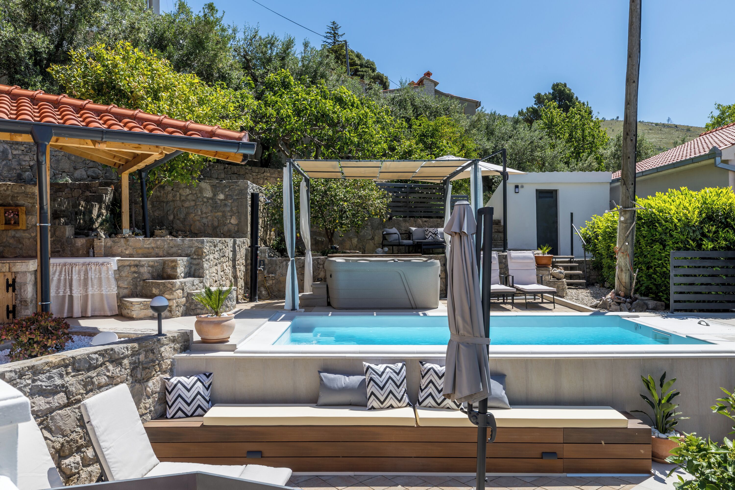 A swimming pool with a wooden deck, outdoor seating, and a stone wall.