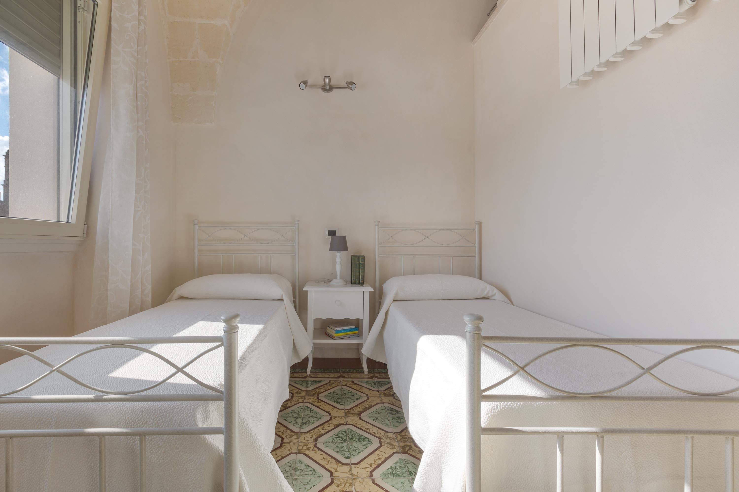 Una habitación pequeña con dos camas individuales, una mesita de noche con lámpara y suelo estampado.