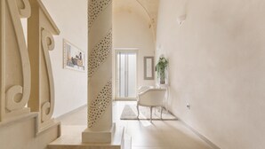 A staircase with a decorative balustrade leading to a room with a chair and a framed picture on the wall. - San Pancrazio Suite Apartments (San Pancrazio Salentino)