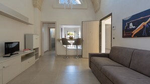 A modern living room with a sofa, TV, and a dining area with chairs and a table. - San Pancrazio Suite Apartments (San Pancrazio Salentino)