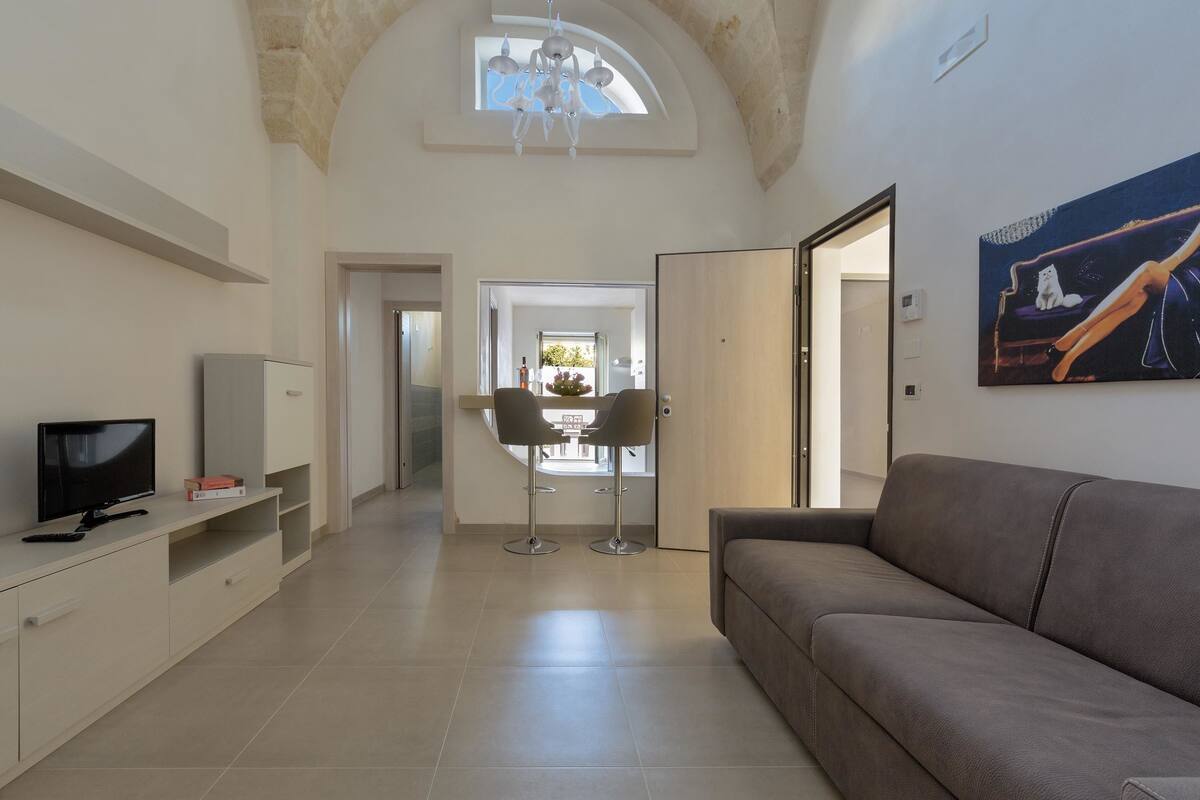 A modern living room with a sofa, TV, and a dining area with chairs and a table.