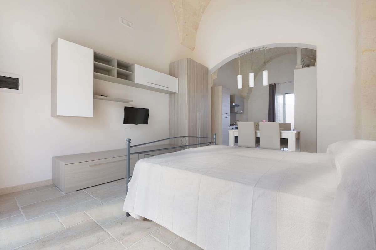 A modern bedroom with a large bed, built-in wardrobe, and a bathroom visible through an archway.
