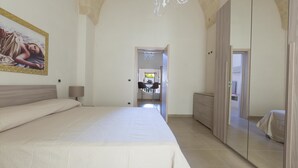 A bedroom with a large bed, a wardrobe, and a mirror. There is a painting on the wall and a chandelier. - San Pancrazio Suite Apartments (San Pancrazio Salentino)