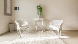 A room with two white upholstered chairs, a white rug, a small white table with a vase of greenery, and a framed picture on the wall. - San Pancrazio Suite Apartments (San Pancrazio Salentino)