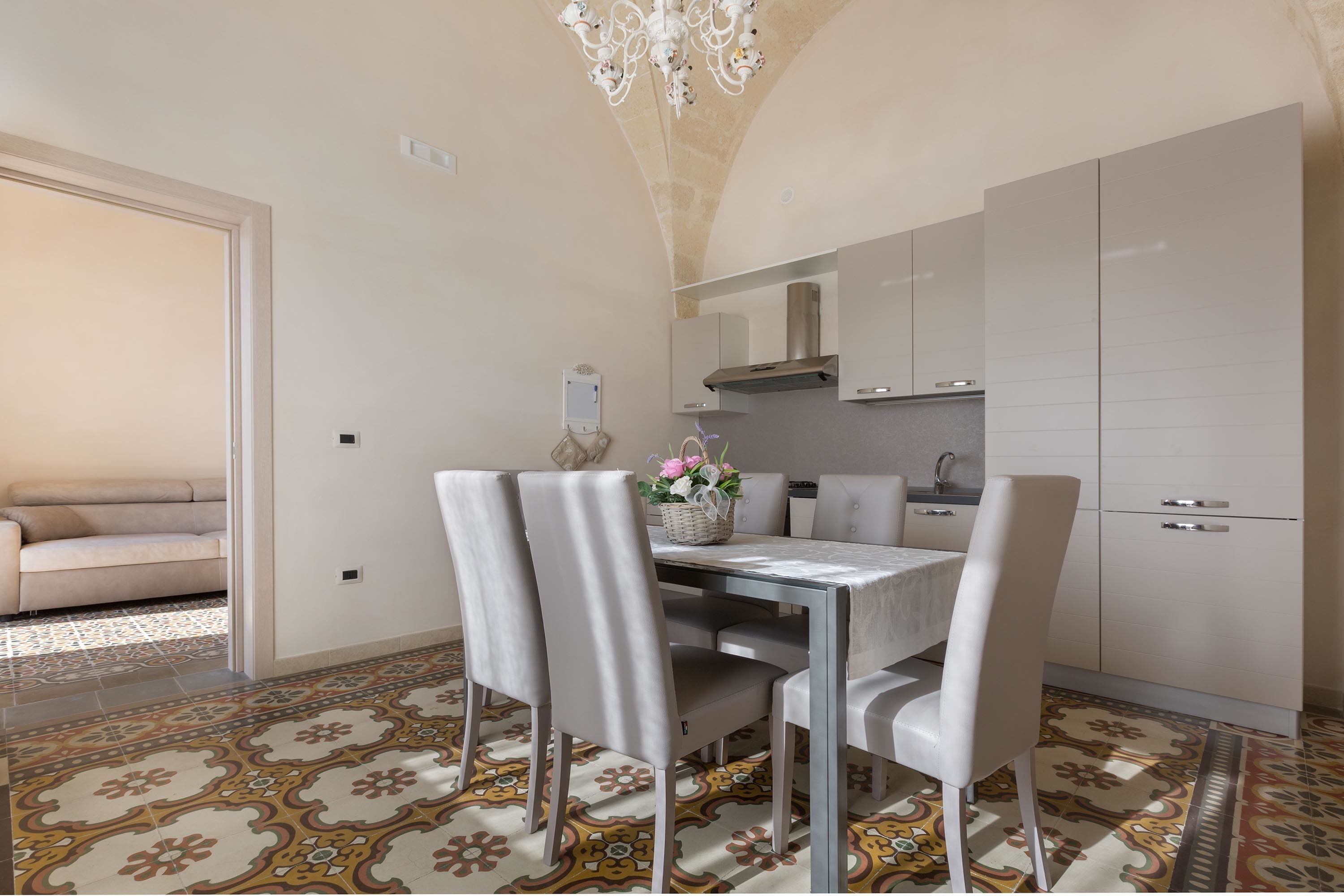 A modern kitchen with white cabinets, a dining table with chairs, and a patterned floor.