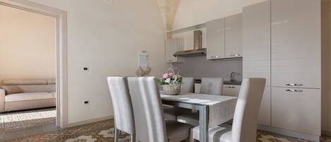 A modern kitchen with white cabinets, a dining table with chairs, and a patterned floor.