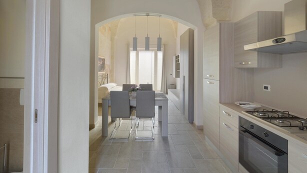 A modern kitchen with a central island, built-in appliances, and a dining area with chairs and a table. - San Pancrazio Suite Apartments (San Pancrazio Salentino)