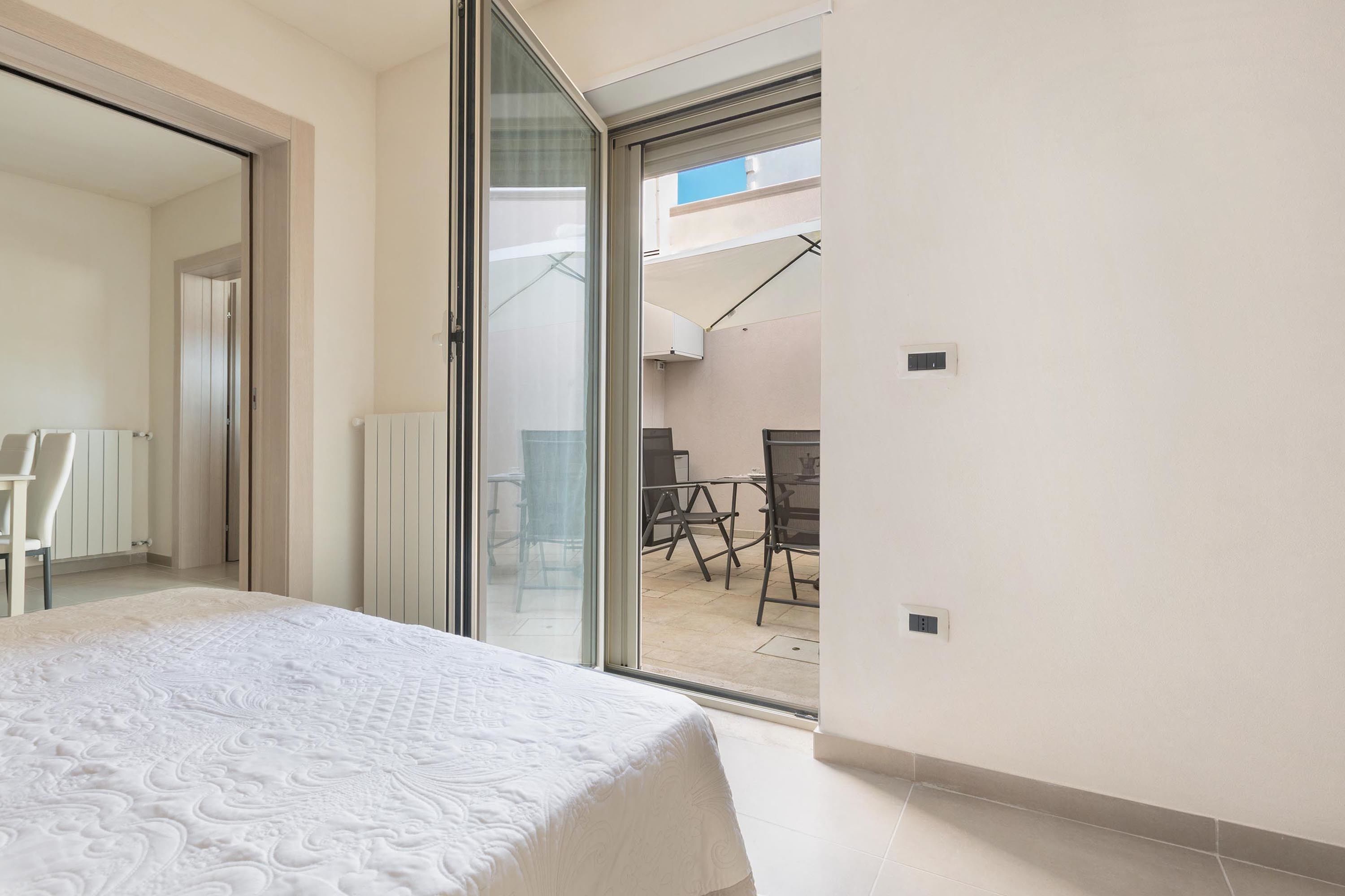 Un dormitorio con una cama grande, un ventanal corredero que da a un balcón con mesa y sillas.