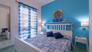 Una camera da letto con un letto, un comodino, una lampada, una parete blu e una finestra con tenda blu.