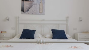 Un letto bianco con due cuscini, una testiera bianca e un comodino con un libro.
