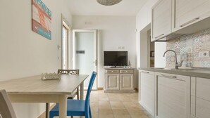 Una cucina compatta con pensili bianchi, un tavolo da pranzo con sedie blu e una televisione a parete.