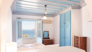 A bedroom with a bed, a dresser, a mirror, and a view of the sea through an open window. - Patmos Sea View Studios (Studio) (Patmos)