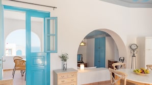 A room with a blue door, a white dresser, a wooden chair, and a table with a fruit bowl. - Patmos Sea View Studios (Studio) (Patmos)
