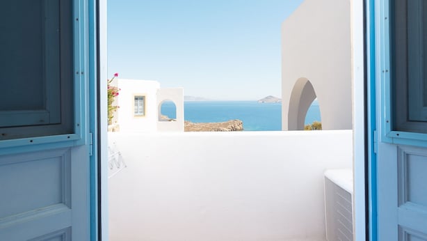 A view from a room with white walls and blue trim, looking out to a coastal landscape with clear skies. - Patmos Sea View Studios (Studio) (Patmos)