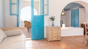 A room with a large blue door, a white sofa, a wooden dresser, and a small table with a plant. - Patmos Sea View Studios (Studio) (Patmos)