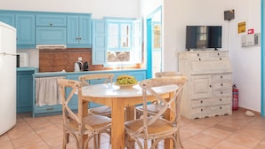 A kitchen with blue cabinets, a round table with chairs, a television, and a fire extinguisher. - Patmos Sea View Studios (Studio) (Patmos)