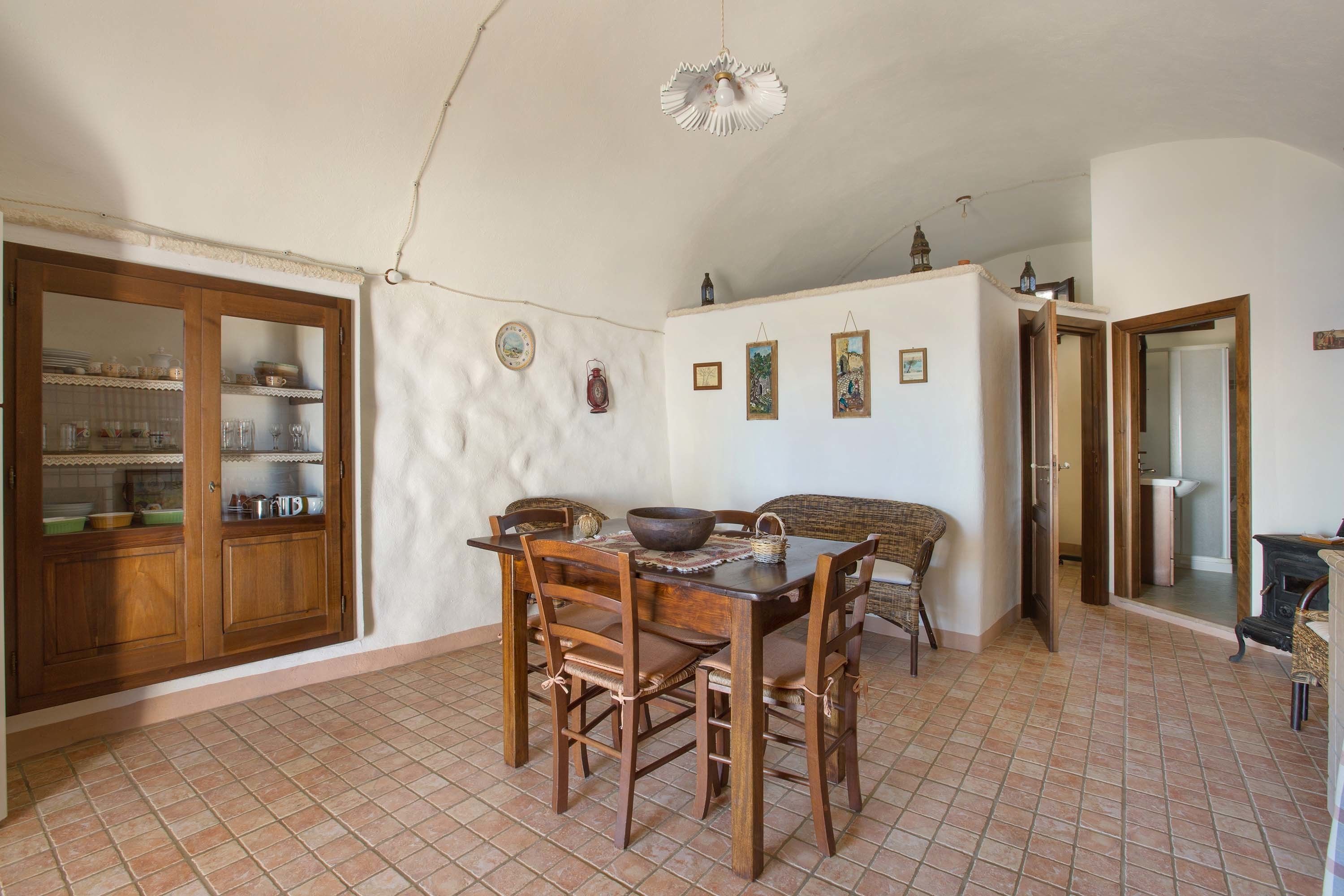 A dining area with a wooden table and chairs, a kitchen with cabinets and shelves, and a bathroom visible through an open door.