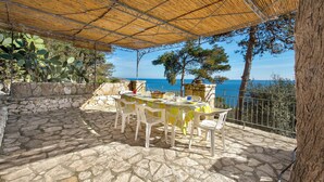 An outdoor patio with a table set for dining, stone flooring, and a view of the sea. - Pajara Acquaviva (Castro)