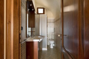 Une petite salle de bain avec une porte en bois, un lavabo blanc, un miroir et des toilettes.