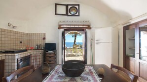 A dining area with a table set for two, a view of the sea through an open door, and a kitchen with tiled backsplash and appliances. - Pajara Acquaviva (Castro)