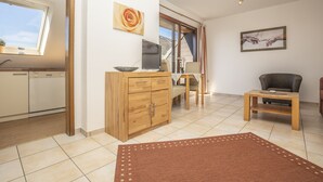 A modern living room with a wooden cabinet, a laptop on a desk, a sofa, and a dining table. - Apartment with sea views (Grömitz)