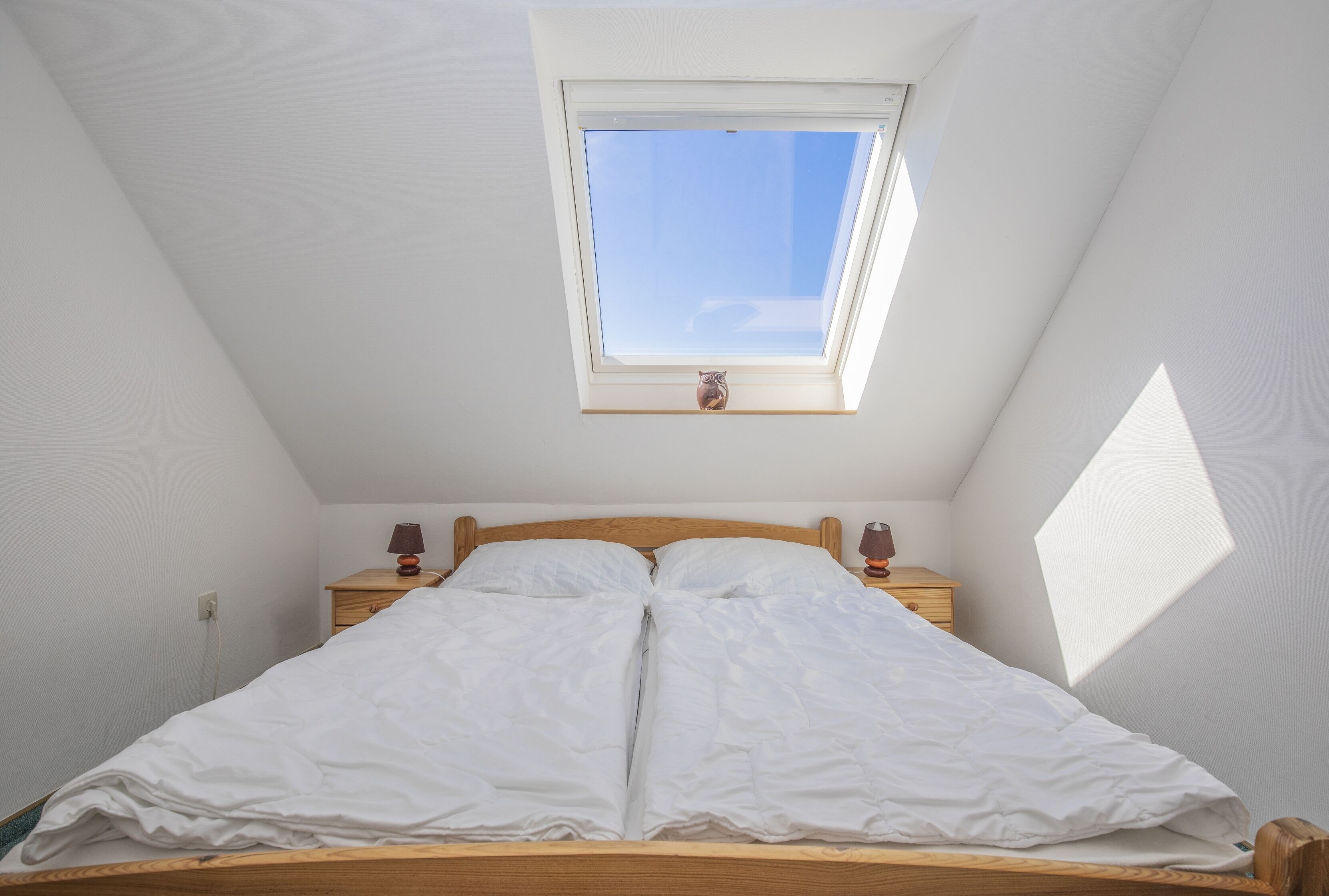 A bedroom with a skylight, a wooden bed frame, two bedside tables with lamps, and a small nightstand.