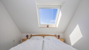 A bedroom with a skylight, a wooden bed frame, two bedside tables with lamps, and a small nightstand. - Apartment with sea views (Grömitz)
